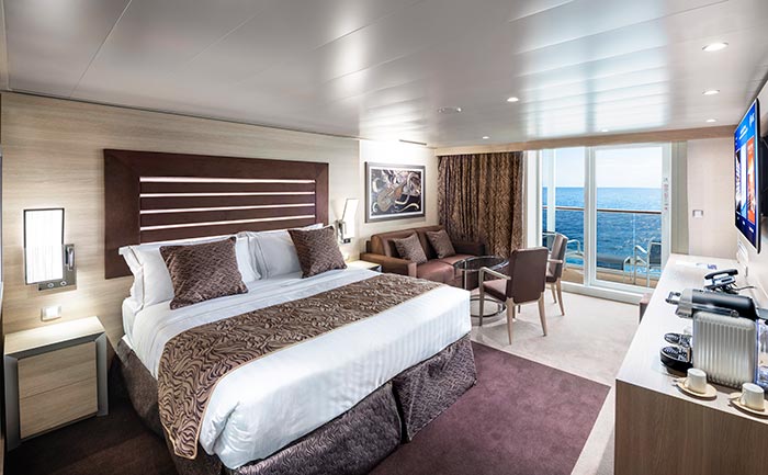 Elegant cruise suite with king-size bed, seating area, and private balcony overlooking the ocean | MSC Cruises