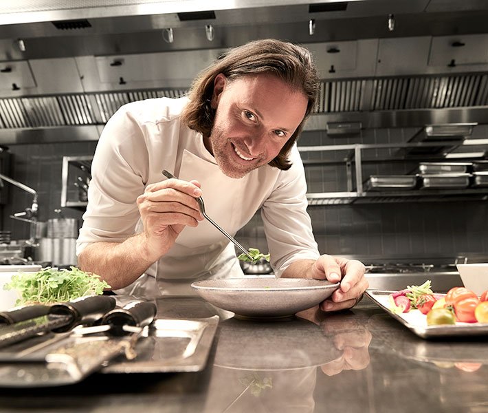 A chef plating a gourmet dish in a modern kitchen | MSC Cruises A chef plating a gourmet dish in a modern kitchen | MSC Cruises