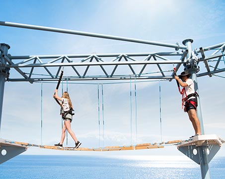 Guests enjoying a ropes course adventure over the ocean under a clear blue sky | MSC Cruises