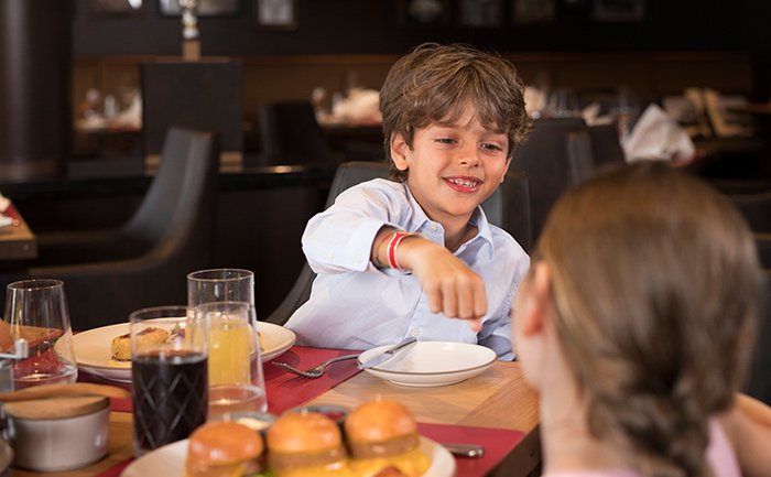 Children enjoying a family meal with burgers and drinks in an elegant onboard restaurant | MSC Cruises Children enjoying a family meal with burgers and drinks in an elegant onboard restaurant | MSC Cruises