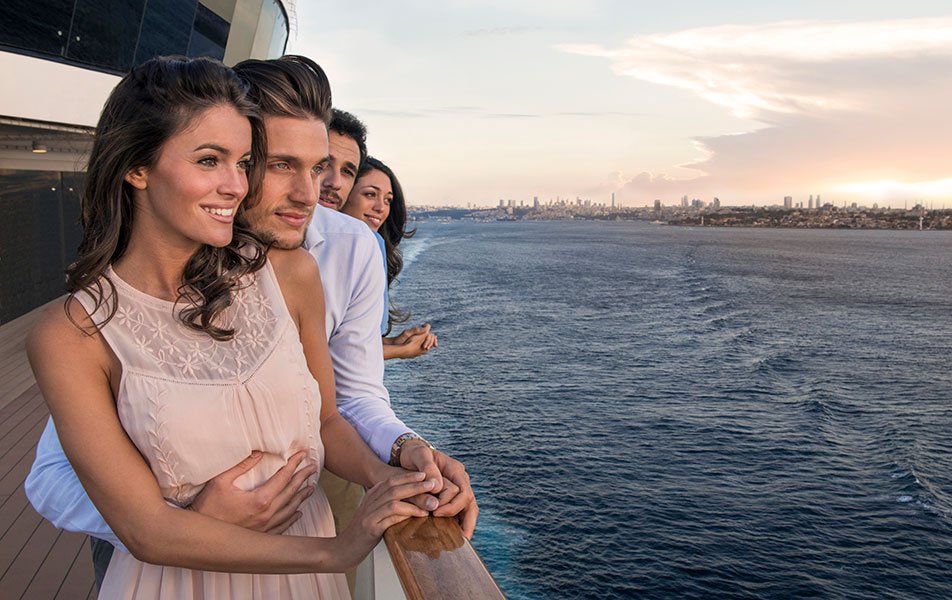 A couple enjoying ocean views from a cruise ship deck at sunset with a city skyline in the distance | MSC Cruises